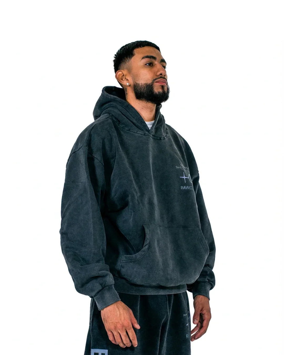 Man wearing dark gray oversized hoodie with kangaroo pocket and matching sweatpants against white background