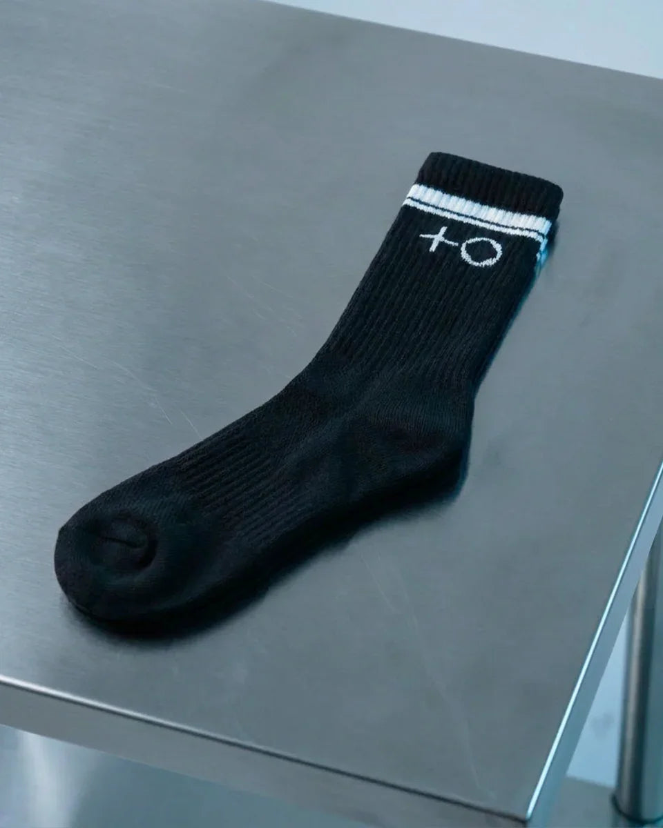 Single black ribbed sock with white stripes and symbols on cuff laid on metallic surface