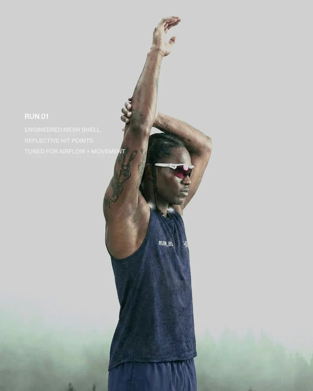 Runner stretching arms wearing navy mesh tank top and sporty sunglasses against foggy background