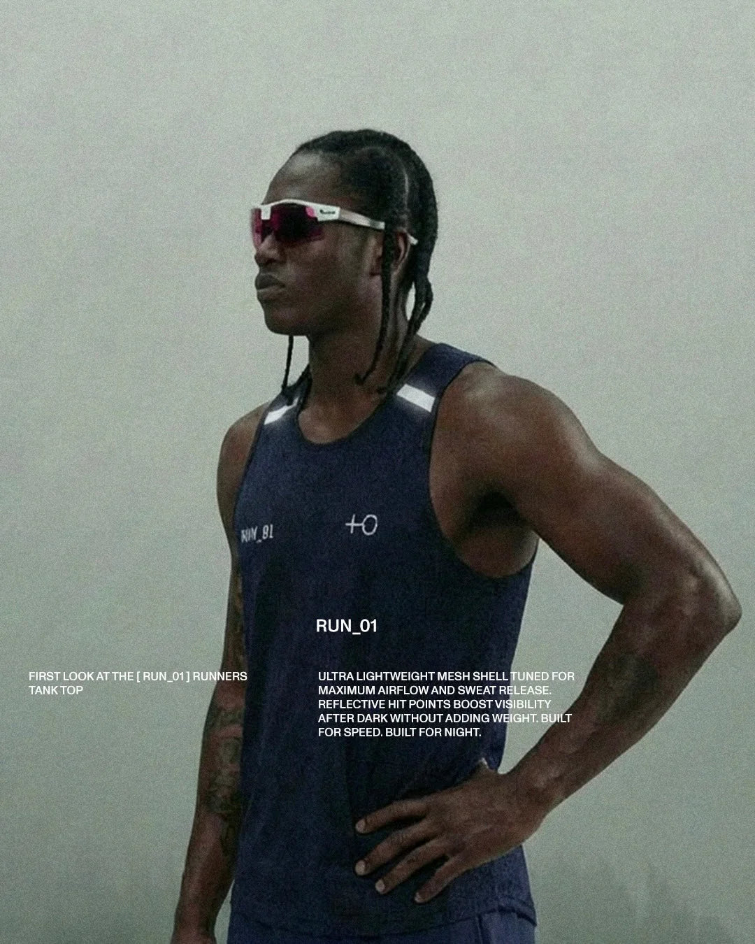 Athletic man wearing navy blue RUN_01 reflective mesh tank top and sunglasses against gray background