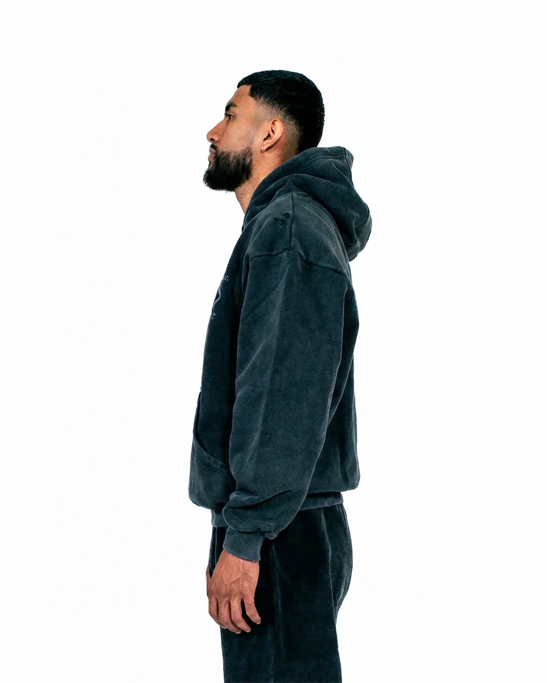 Side view of man wearing dark gray hooded sweatshirt and matching pants on white background