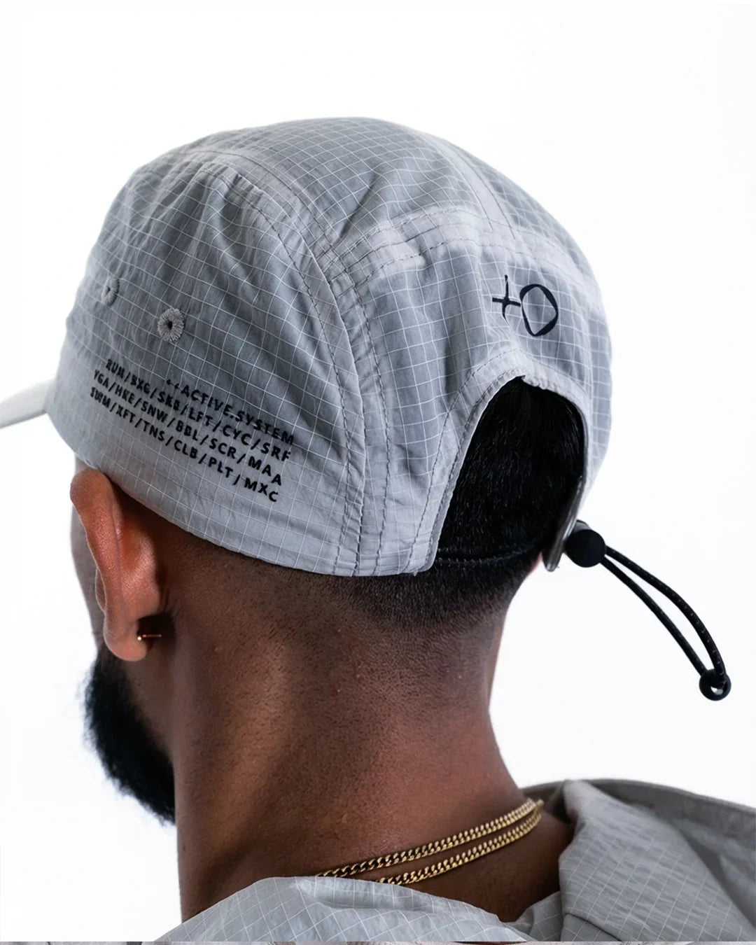 Back view of man wearing light gray ripstop fabric cap with black text and adjustable cord detail