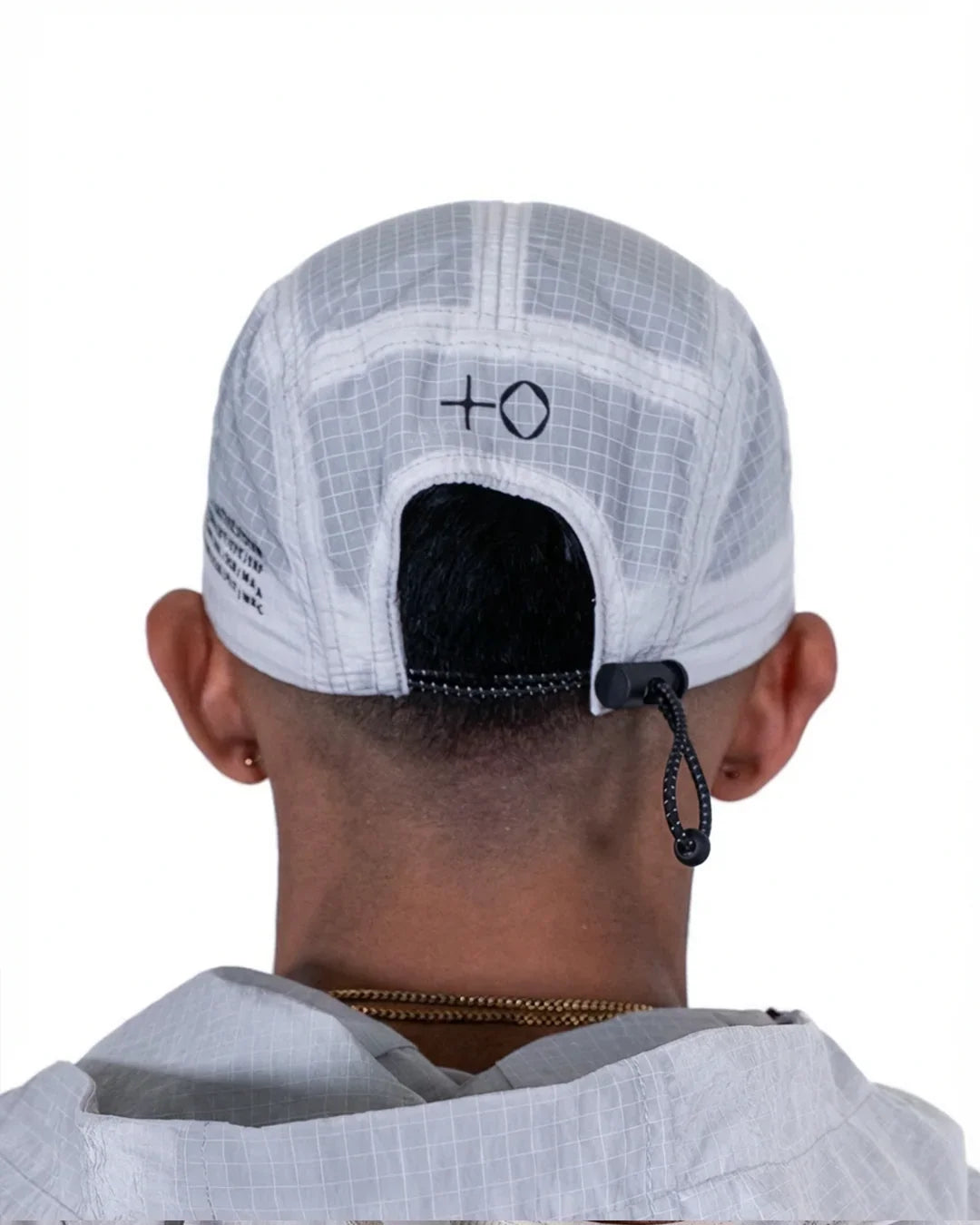 Back view of a person wearing a white grid-patterned adjustable cap with a black cord lock and a small plus zero logo