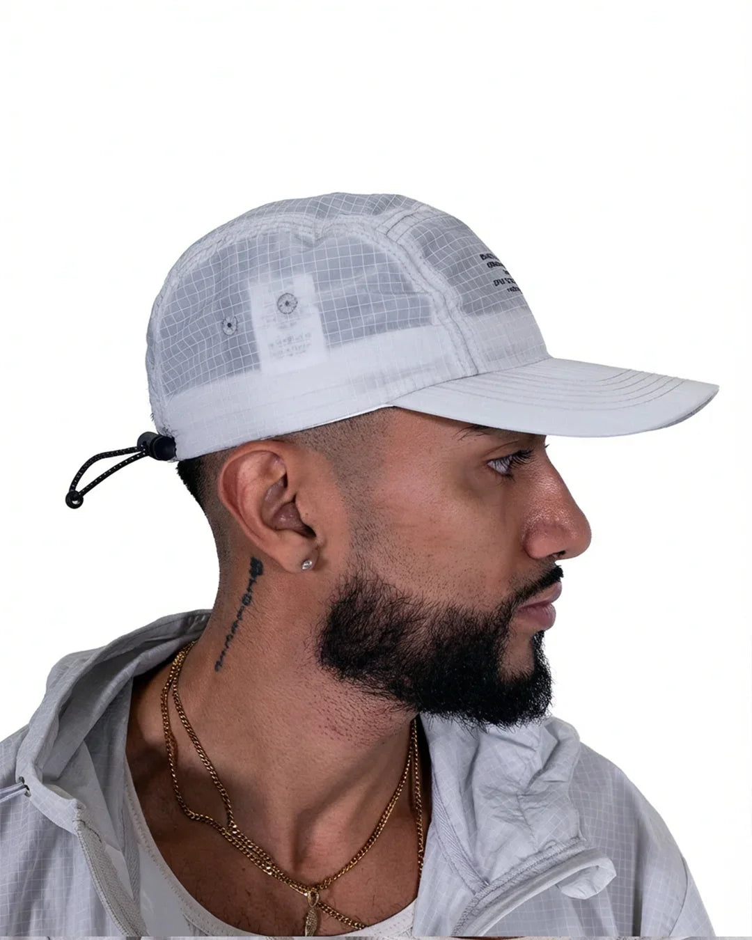 Side profile of man wearing white grid-patterned lightweight cap with adjustable back strap and matching jacket