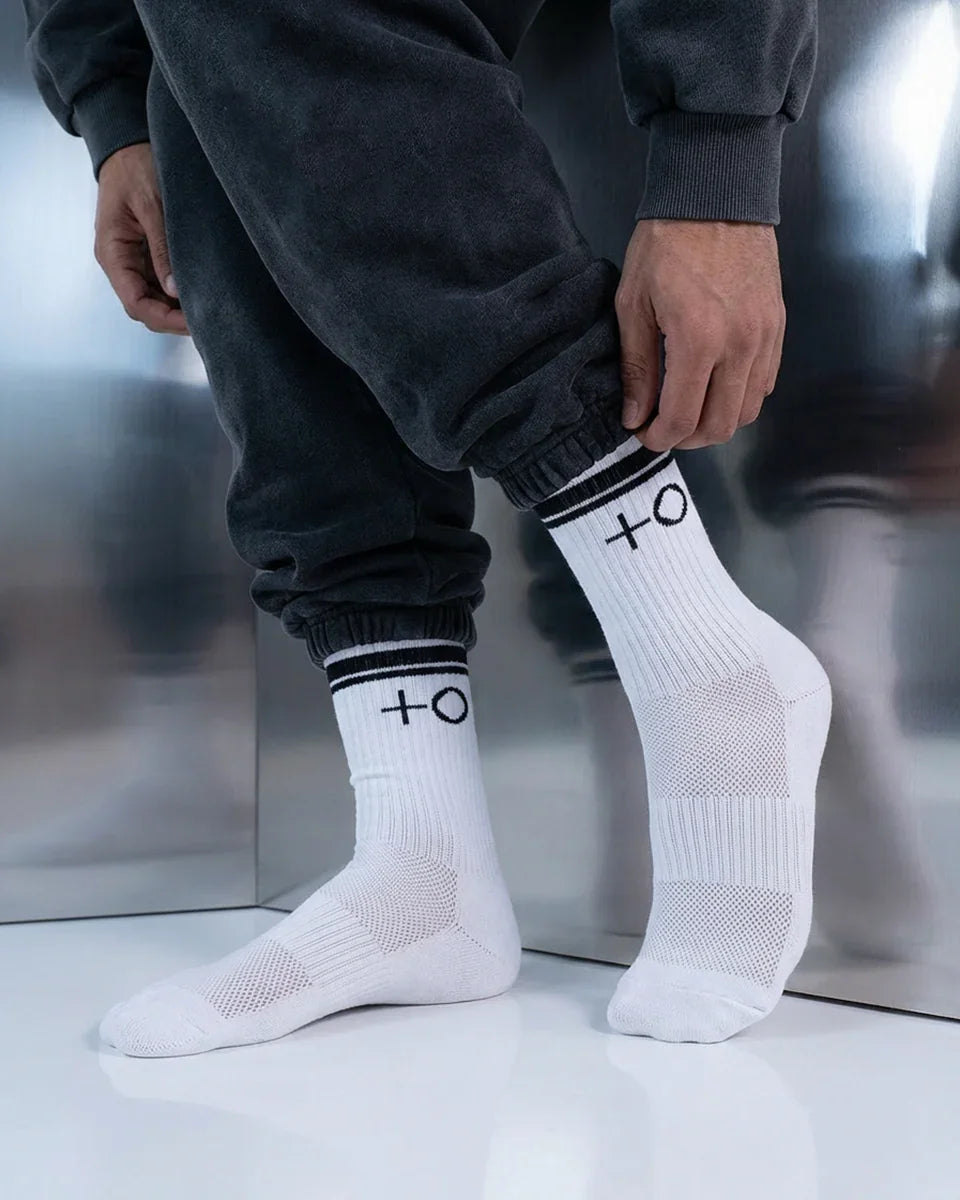 Person wearing white ribbed socks with black stripes and symbols, paired with black sweatpants