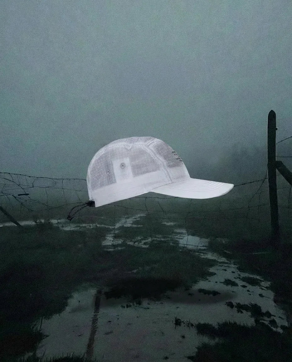 White mesh trucker cap floating over dark, foggy outdoor scene with a broken wire fence