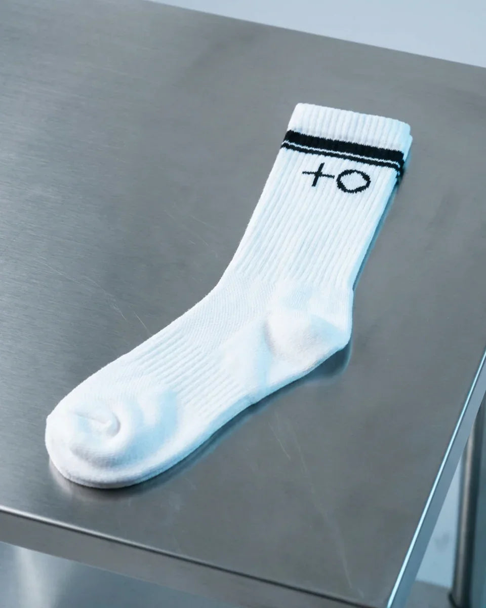 White ribbed crew sock with black stripes and plus circle logo on metal surface