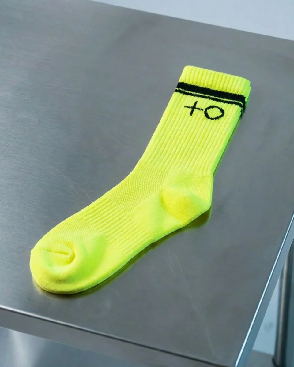 Neon yellow crew sock with black stripes and symbols on a metallic surface